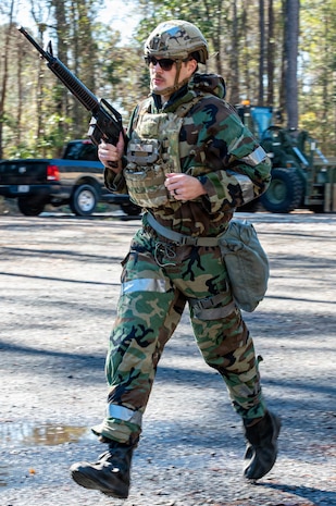 An Airman holding a training weapon runs across a clearing.
