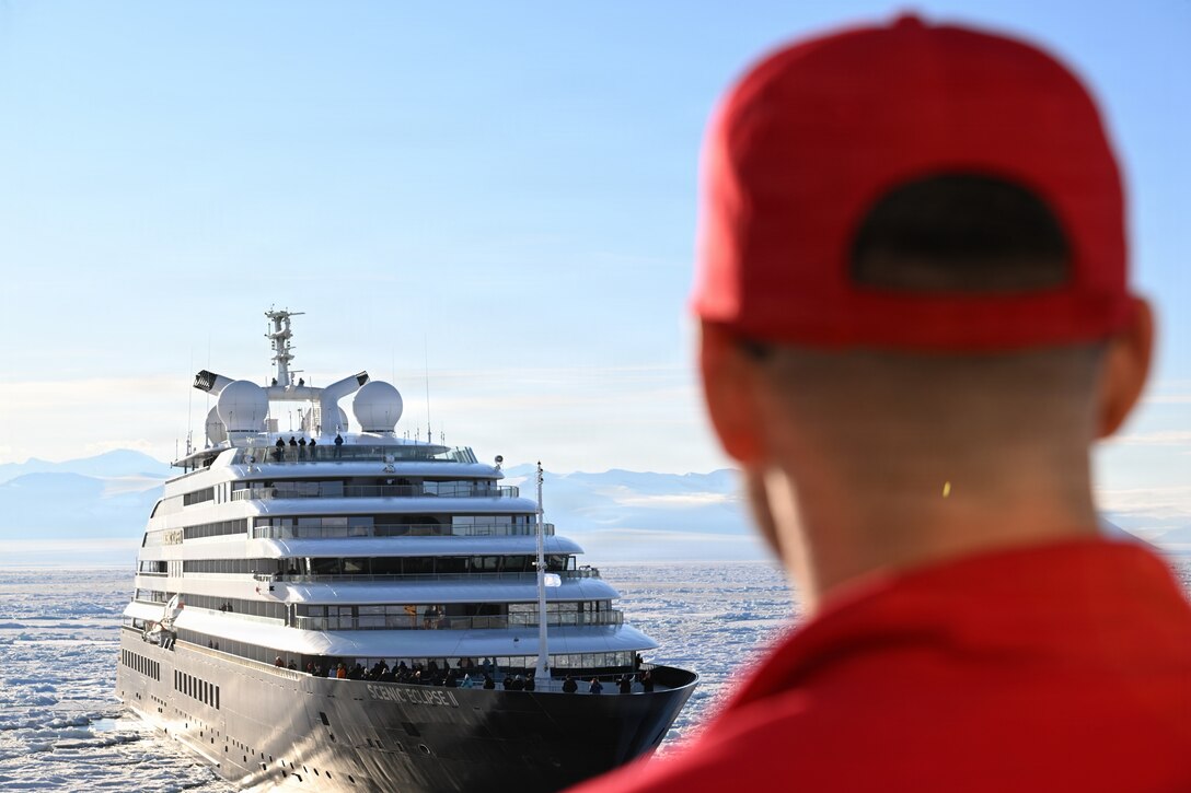 A USCGC Polar Star (WAGB 10) crew member looks on at an Australian-owned cruise ship being escorted out of the Ross Sea after requesting assistance to depart the ice on the cutter’s 50th birthday, Jan. 17, 2026 during Operation Deep Freeze 2026. The U.S. Air Force, Army, Coast Guard, and Navy contribute unique capabilities to the success of this mission, providing strategic inter-theater airlift, tactical deep field support, aeromedical evacuation support, search and rescue response, sealift, seaport access, bulk fuel supply, port cargo handling, and transportation requirements. (U.S. Coast Guard photo by Petty Officer 2nd Class Christopher Bokum)