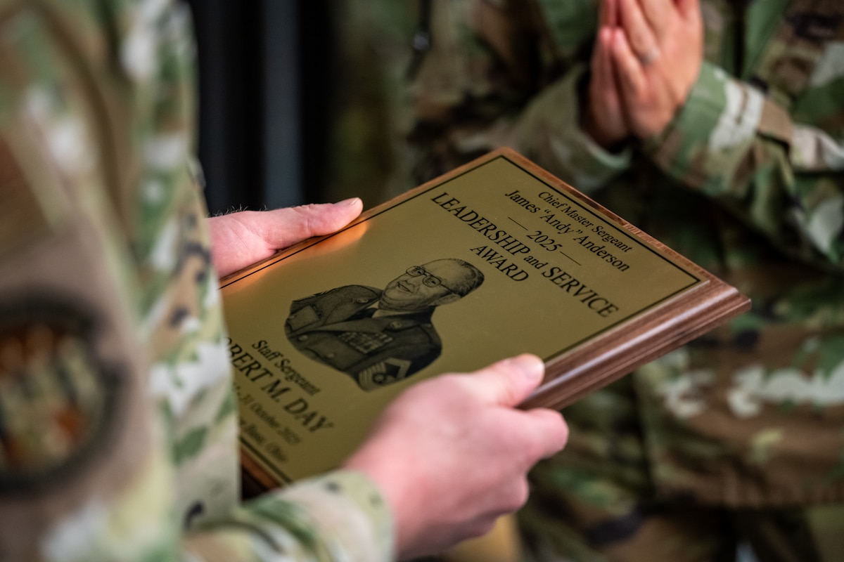 A close-up image of two hands holding an award plaque of wood and brass