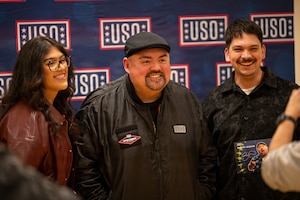 A comedian poses for a photo with people in front of a USO backdrop.