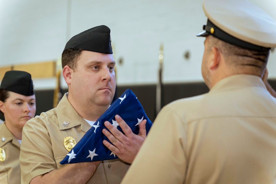 Master-at-Arms 1st Class Michael Morelli, assigned to Naval Support Activity (NSA) Souda Bay, passes the flag to Chief Master-at-Arms Brian Matteson, assigned to NSA Souda Bay, during Matteson’s retirement ceremony onboard NSA Souda Bay, Jan. 9, 2026.