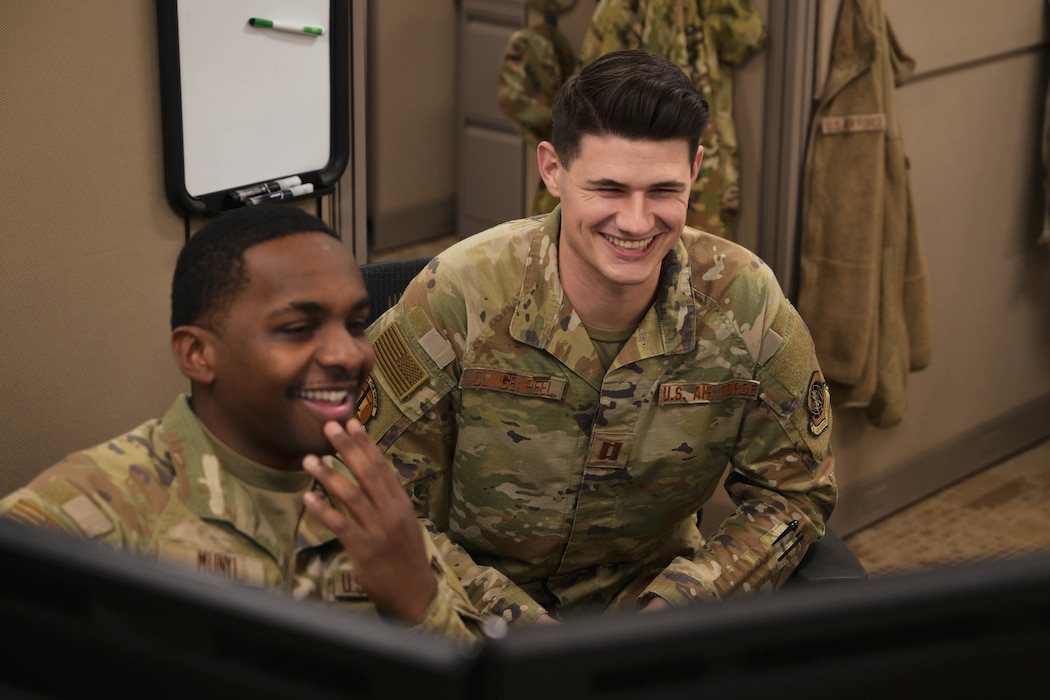 Two men in uniform speak with each other while looking at a computer.
