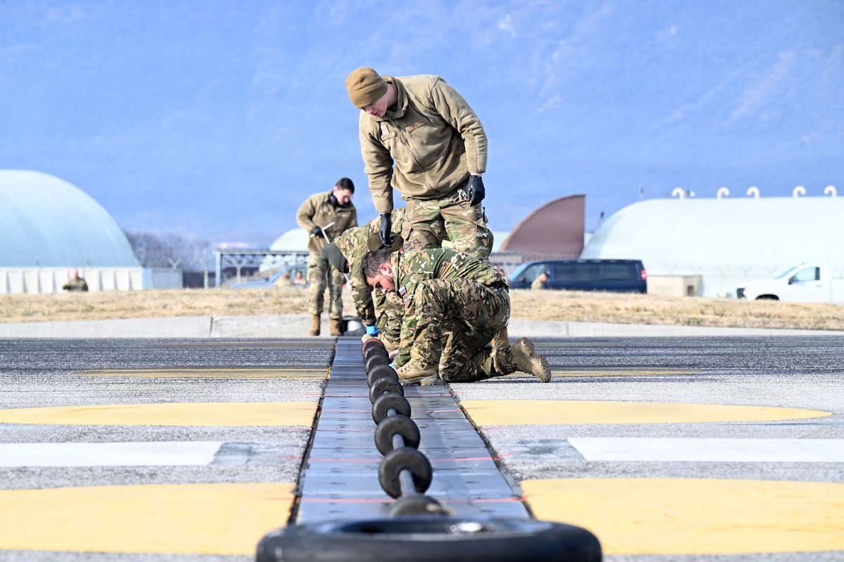 U.S. Air Force Airmen assigned to the 31st Civil Engineer Squadron along with members of the Slovenian armed forces, perform an inspection on the barrier arresting system at Aviano Air Base, Italy, Jan. 9, 2026. The system is designed to stop an aircraft by catching it with a cable during an emergency landing. (U.S. Air Force photo by Airman 1st Class Stephan Bang)