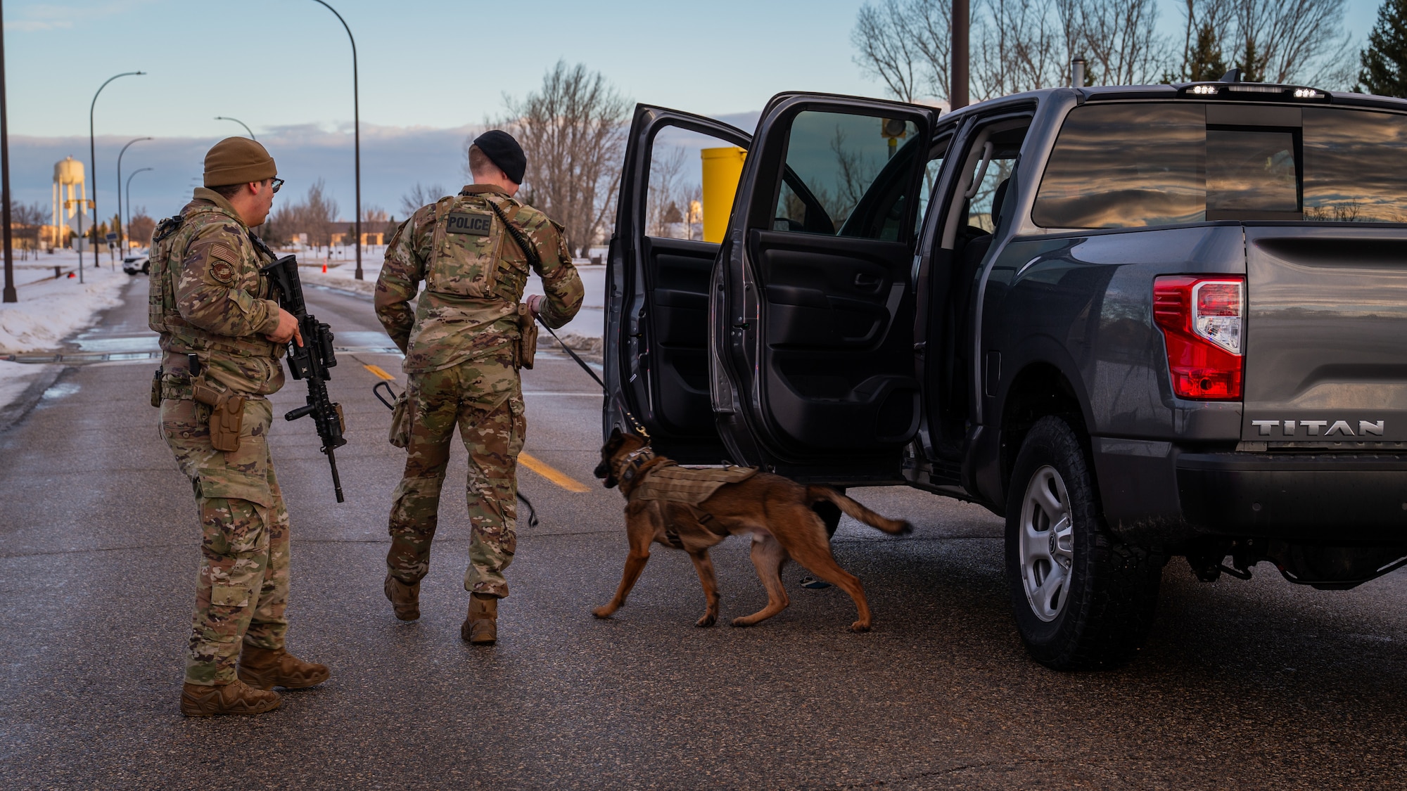A photo of two men standing as a dog searches a vehicle.