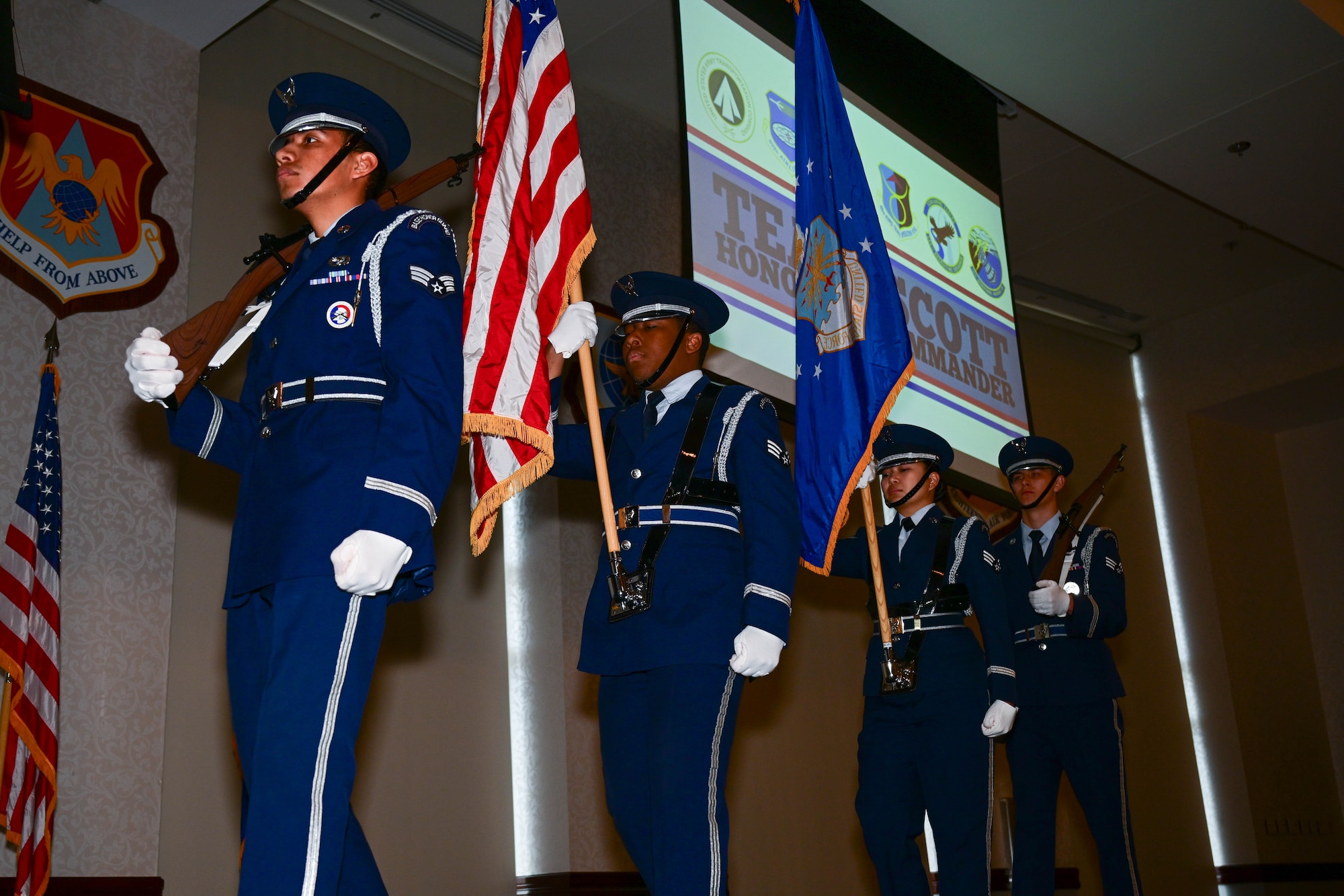 4 Airmen walking on stage, with a U.S. flag, Air Force Flag, 2 rifles, dressed in blues