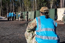 A photo of a woman squatting down outside observing Airmen.