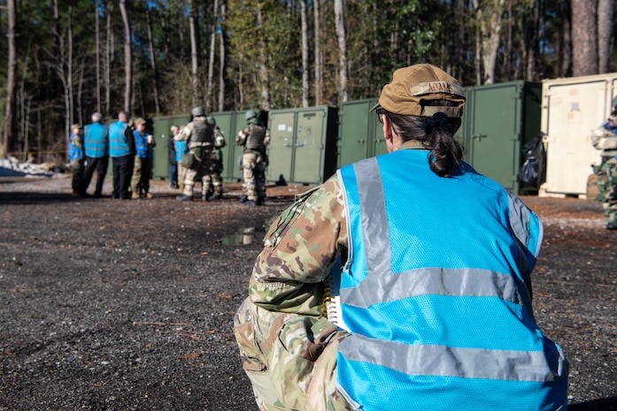 A photo of a woman squatting down outside observing Airmen.