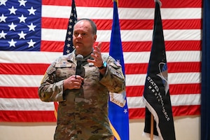 A man stands in front of flags and speaks into a microphone