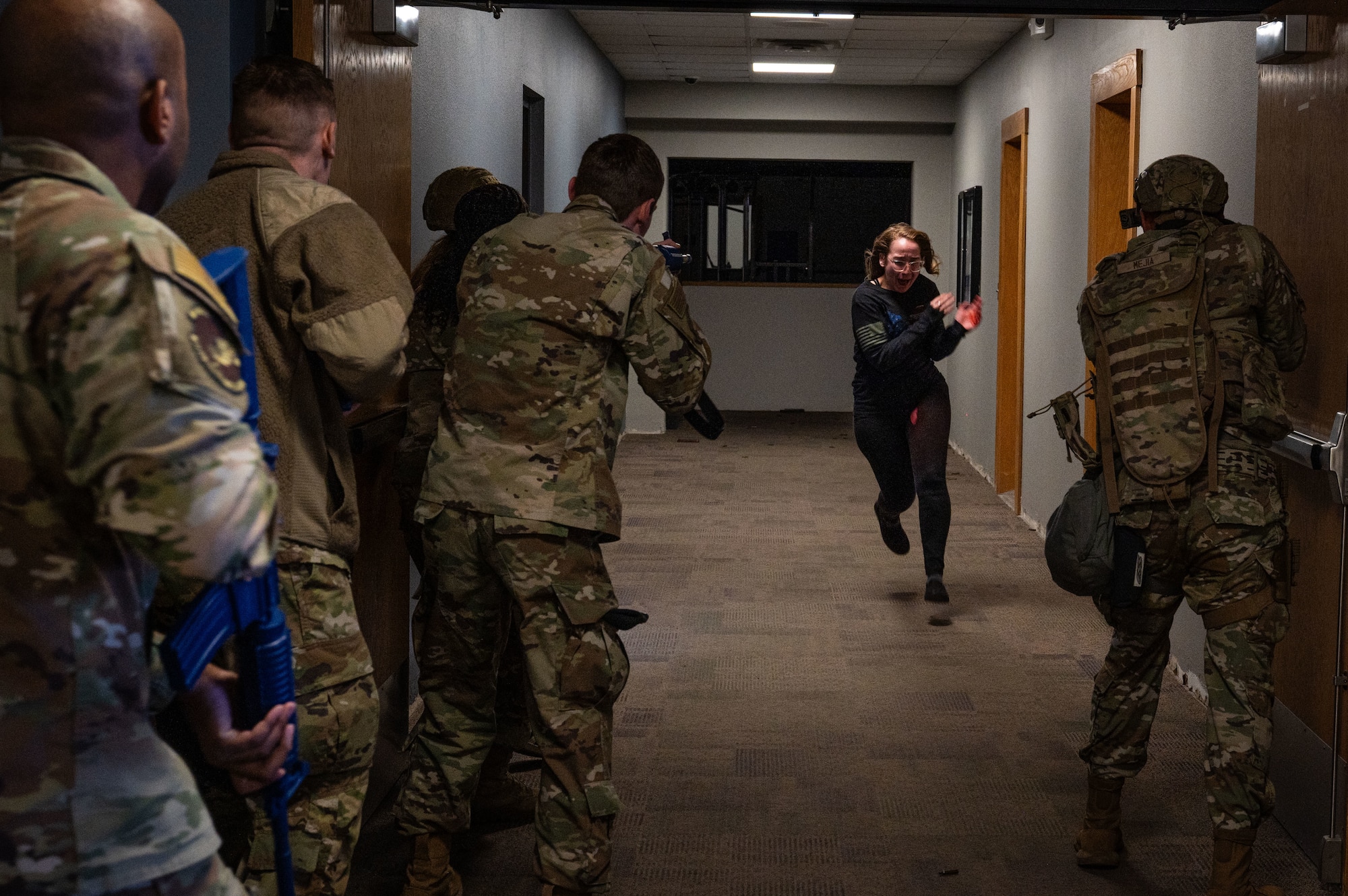 A photo of a group of military members watching as a woman runs down a hall during an active shooter exercise.