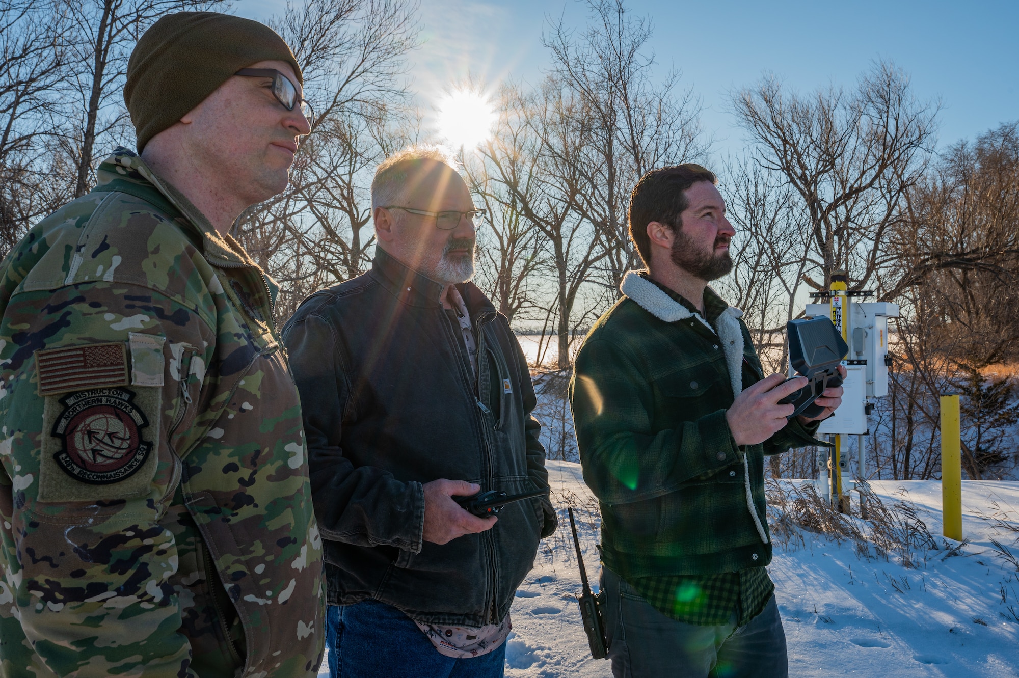 A photo of three men standing next to each other looking at the sky.