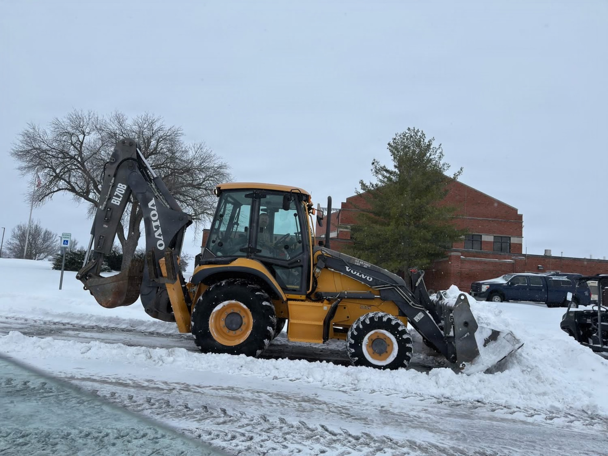 A yellow Volvo front loader moves snow into a pile in a parking lot.