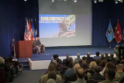 A video is projected on a stage. Leadership sits to the side and employees sit in the audience.