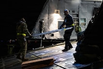 Airmen carry a piece of a ramp out of an aircraft.