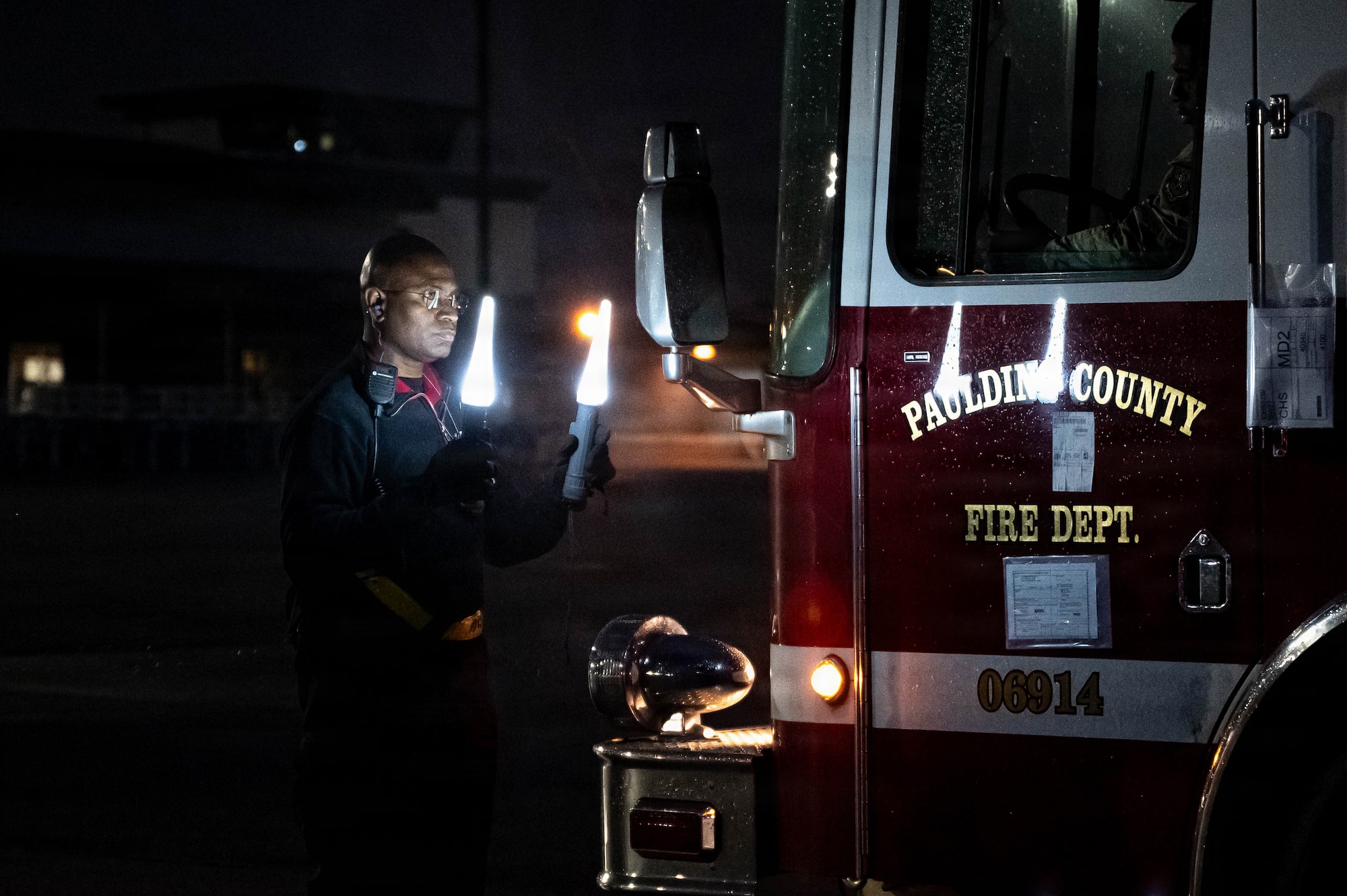 An Airman directs a firetruck to drive backward in the dark