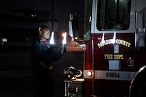 An Airman directs a firetruck to drive backward in the dark