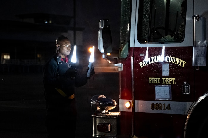 An Airman directs a firetruck to drive backward in the dark