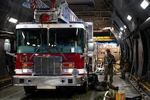 A firetruck sits inside of a C-17 Aircraft with Airmen standing and laying around it.