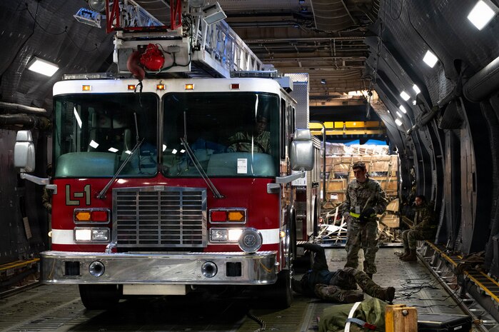 A firetruck sits inside of a C-17 Aircraft with Airmen standing and laying around it.