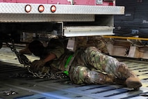 An Airman lays under a firetruck attaching it to the floor of a C-17 aircraft