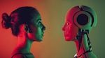 A human woman and a humanoid robot face each other in profile, illuminated by contrasting red and green lighting against a gradient background, suggesting a moment of confrontation or connection between human and artificial intelligence.