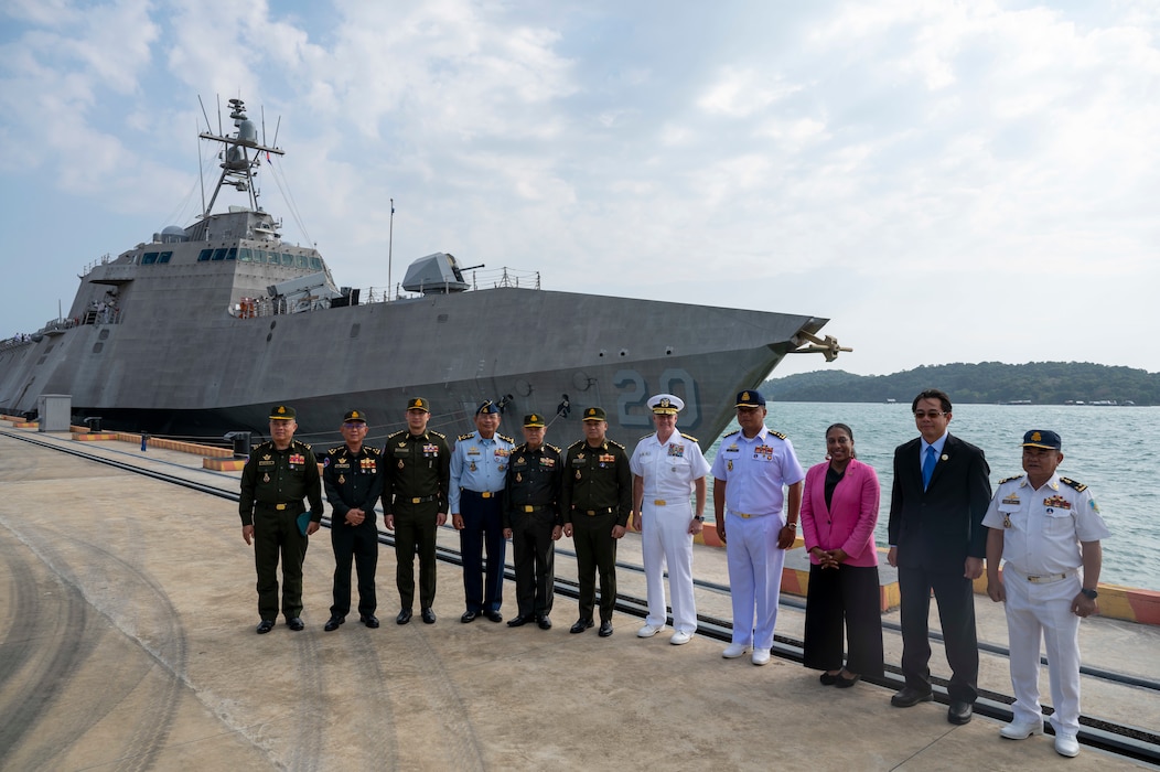 A group of people stand on a pier in front of a warship