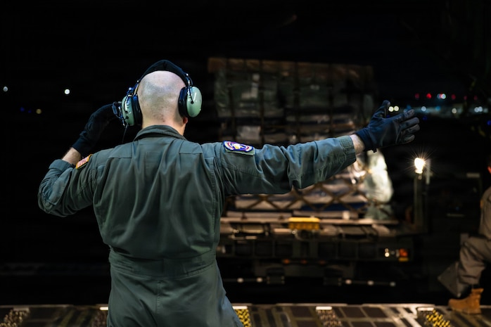 An Airman directs a k-loader holding humanitarian cargo