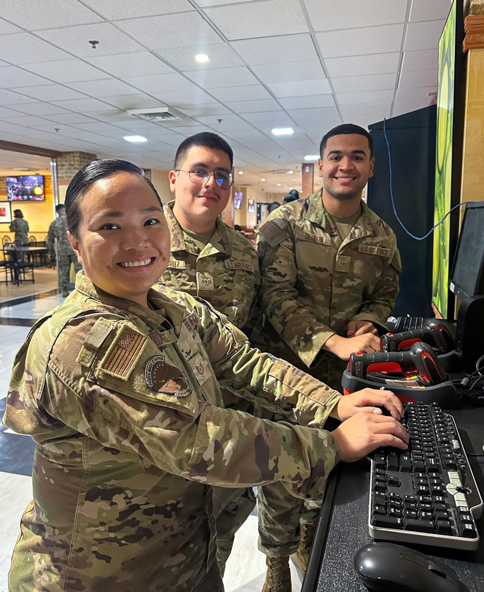 Three Airmen pose for a photo at a computer