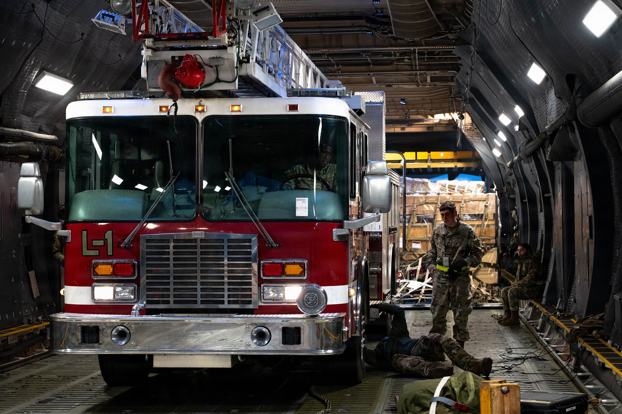 A firetruck sits inside of a C-17 Aircraft with Airmen standing and laying around it.
