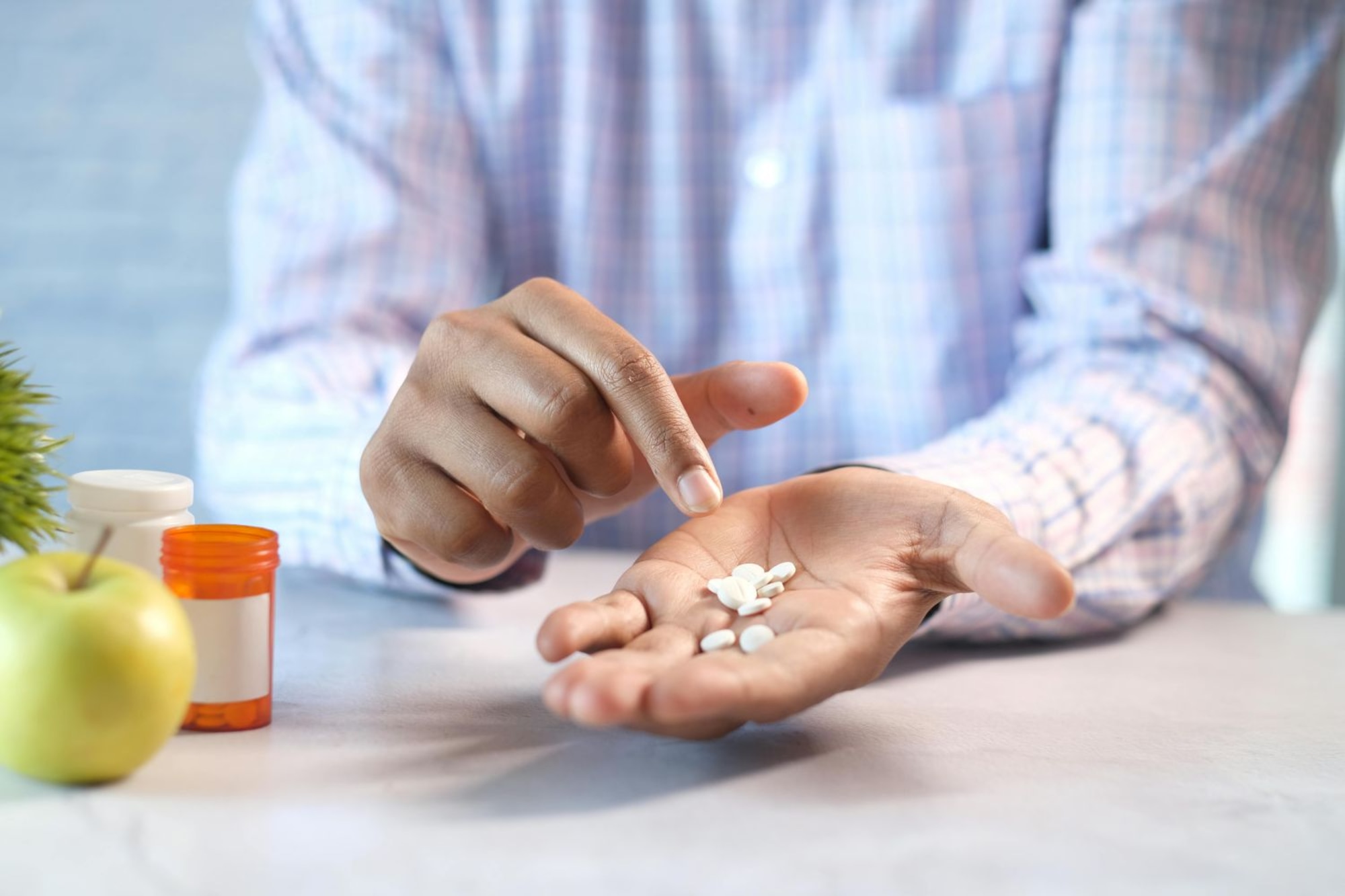Man holds white pills in his hand while he leans over a white countertop