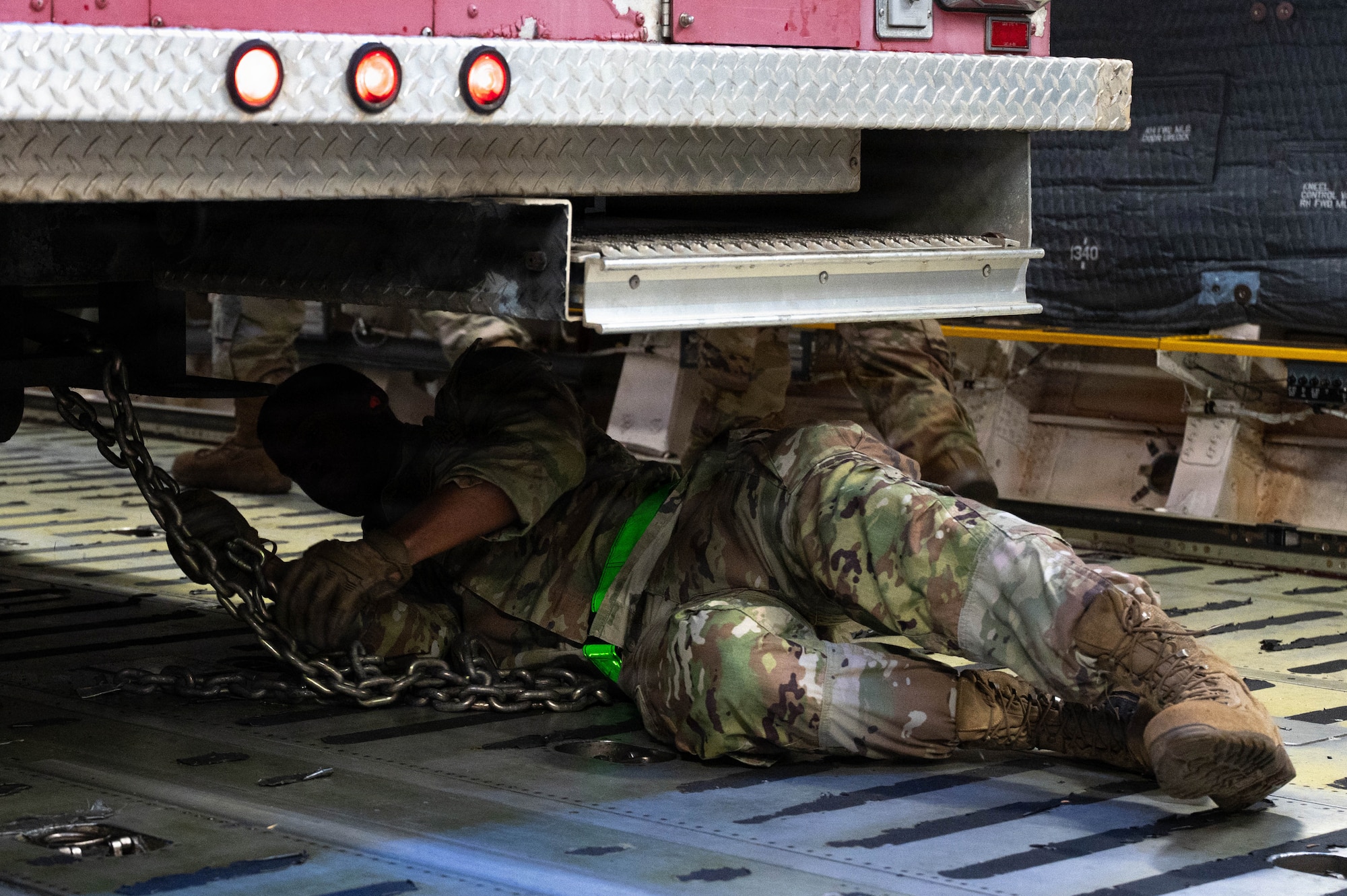 An Airman lays under a firetruck attaching it to the floor of a C-17 aircraft