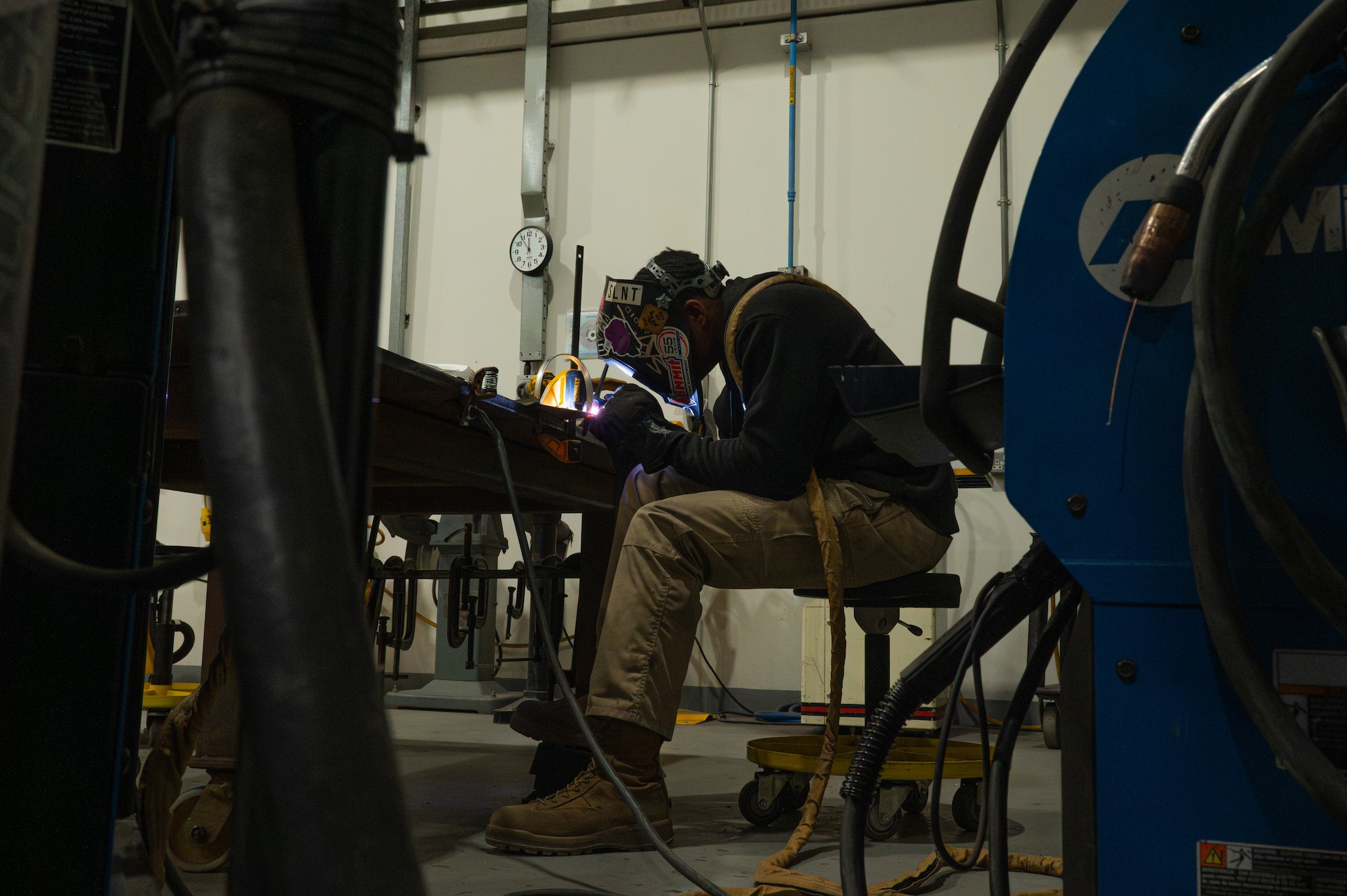 An Airman sits at a table hunched over welding metals together