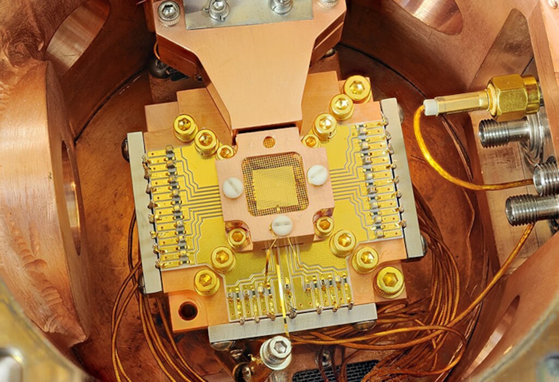 NIST physicists used this apparatus to coax two beryllium ions (electrically charged atoms) into swapping the smallest measurable units of energy back and forth, a technique that may simplify information processing in a quantum computer. The ions are trapped about 40 micrometers apart above the square gold chip in the center. The chip is surrounded by a copper enclosure and gold wire mesh to prevent buildup of static charge.