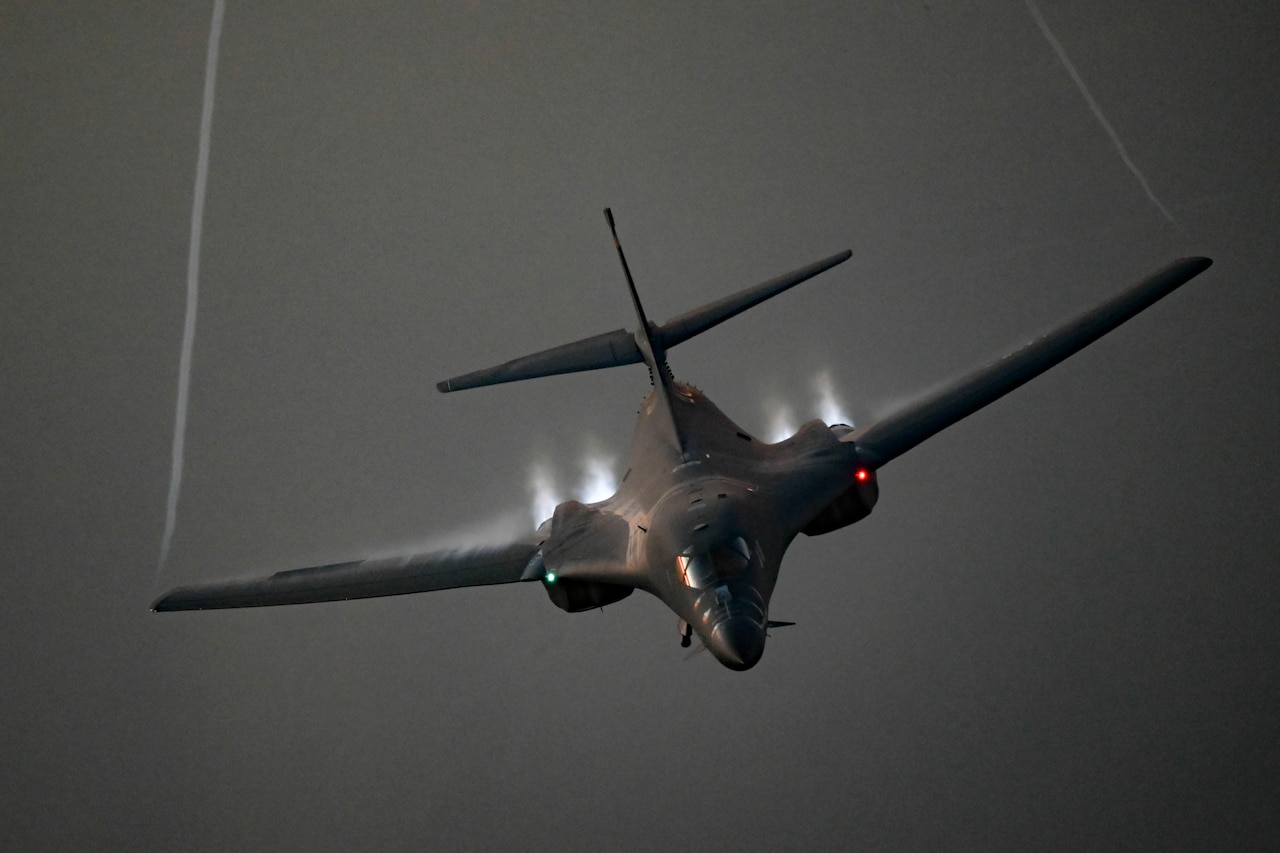 A large military aircraft flies through the air with trial of water vapor coming off the wings.