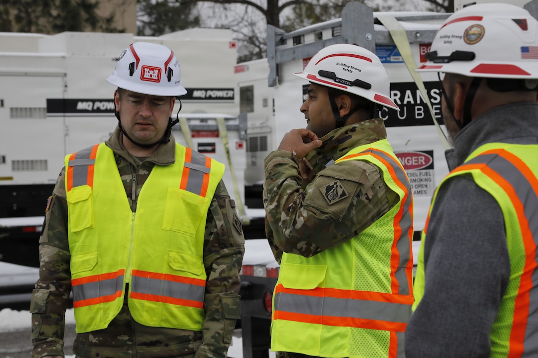 Soldiers in hard hats and protective vests are seen talking with generators in the background