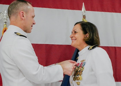 VIRGINIA BEACH, Virginia (Aug. 28, 2025) - Capt. David Cox, chief of staff, commander, Submarine Force, U.S. Pacific Fleet, left, presents an award to Capt. Stephany Moore, outgoing commanding officer, commander, Undersea Surveillance (CUS), right, during a change of command ceremony for CUS held at the Center for Naval Aviation Technical Training Unit in Virginia Beach, Virginia, Aug. 28, 2025. During the ceremony, Capt. Steven Lawrence, from Bridgeport, Pennsylvania, relieved Moore, from Caledonia, New York as commander of CUS. CUS provides global maritime acoustic surveillance and timely, accurate anti-submarine warfare (ASW) reporting using persistent, long-range, fixed and mobile systems. (U.S. Navy photo by Yeoman 1st Class Nikolas Cantu)