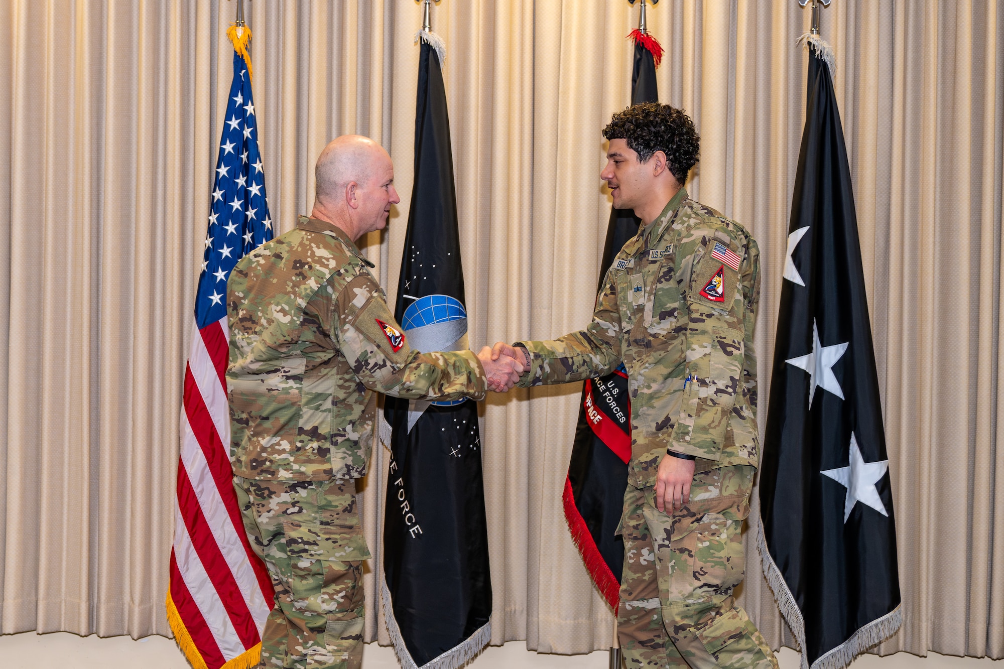 A soldier shakes hands with a general in an auditorium