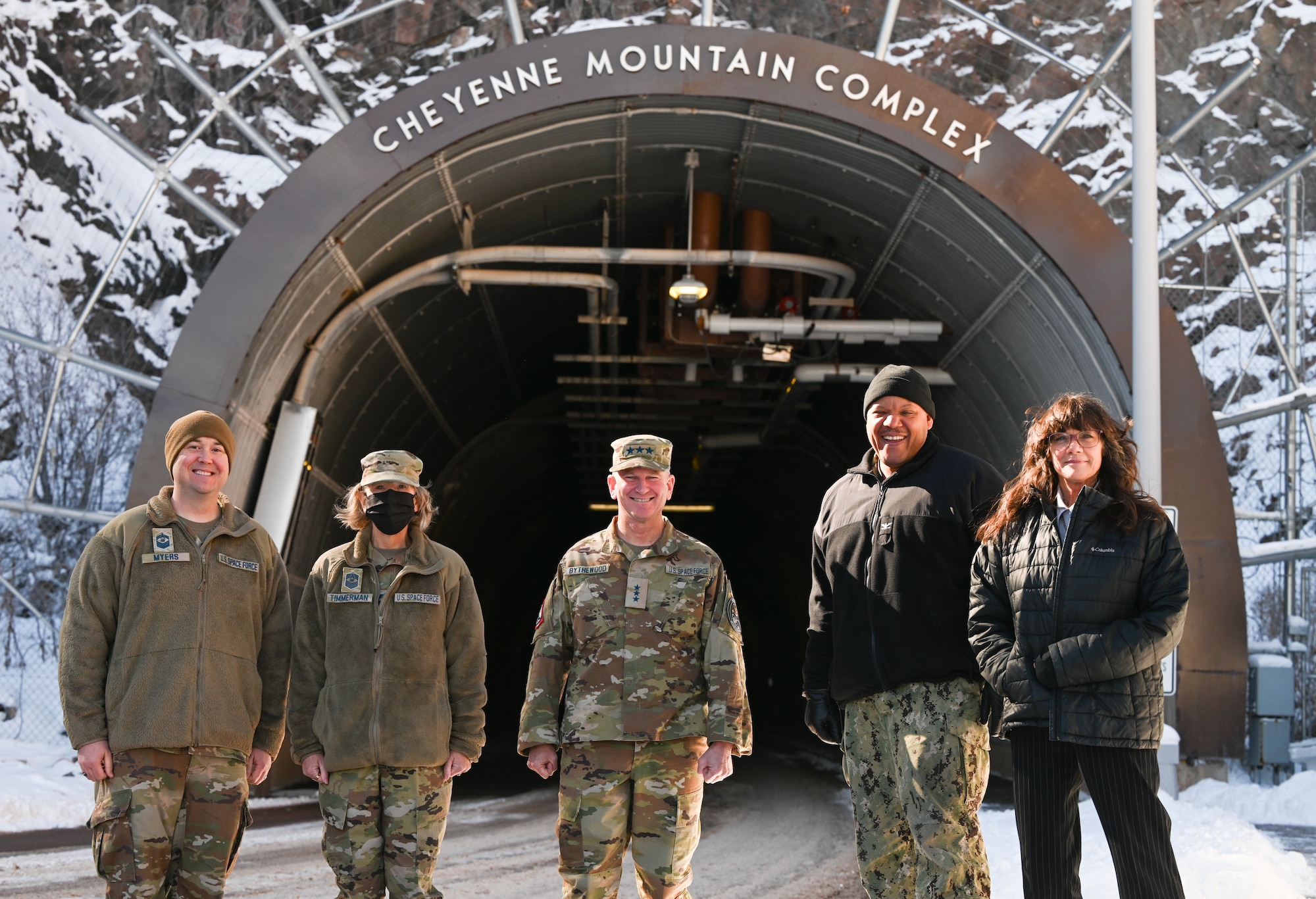Five military members stand in front of a large tunnel in the side of a mountain