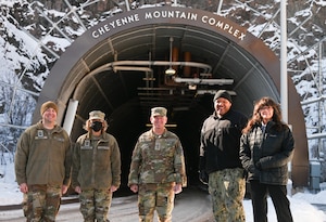 Five military members stand in front of a large tunnel in the side of a mountain