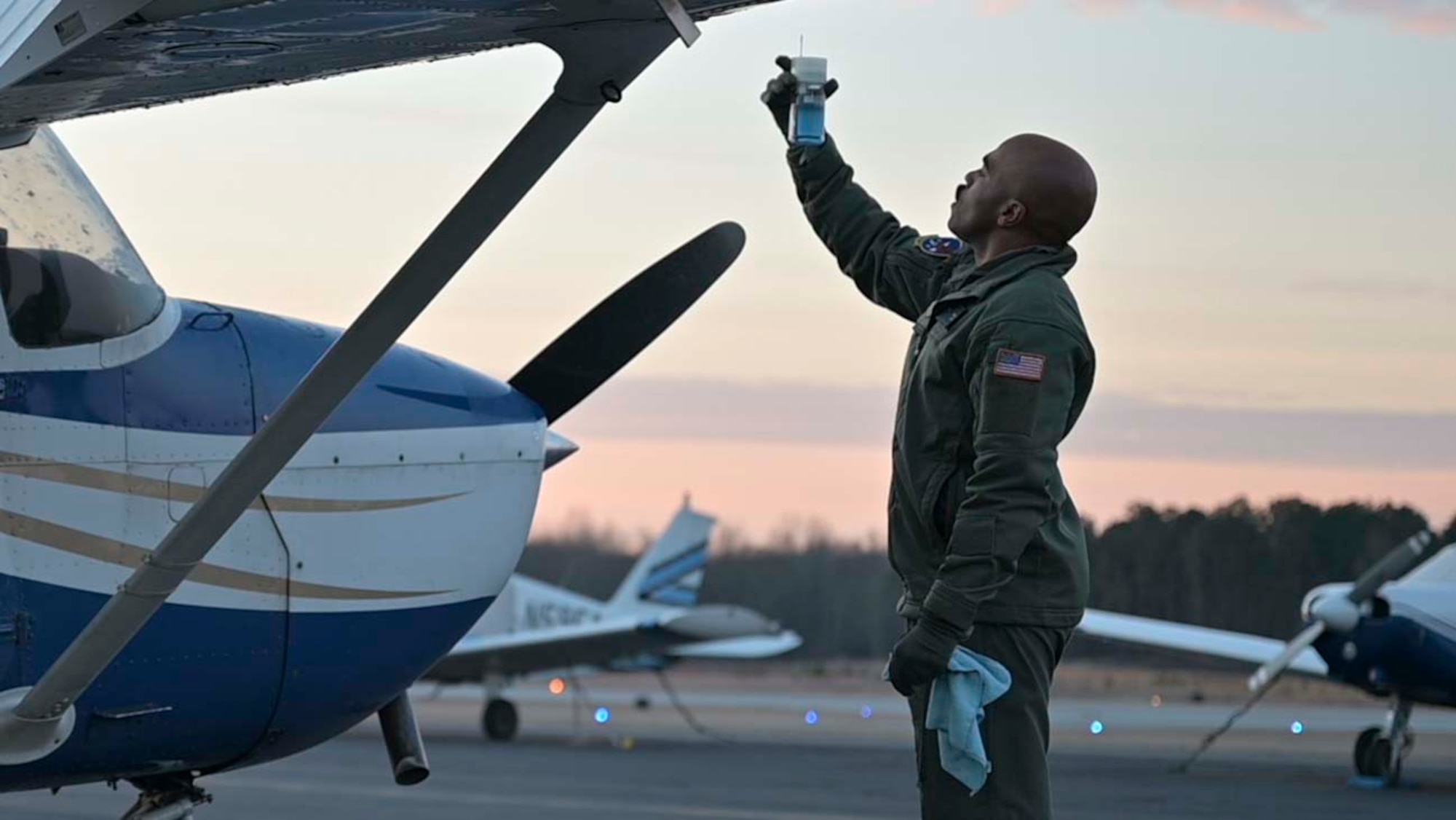 A pilot in training stands in front of a Cessna while testing the fuel of the aircraft.