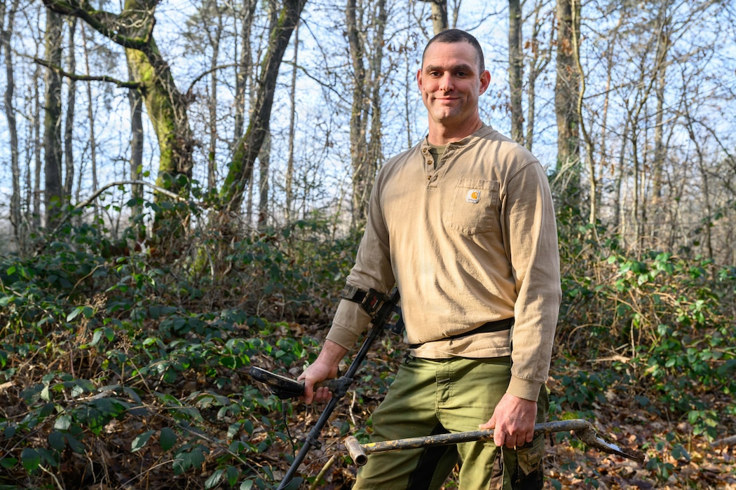 A person poses with his metal detector and shovel.