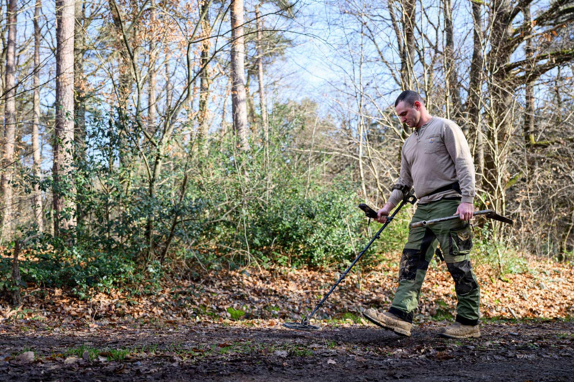 A person is walking in the woods with a metal detector.
