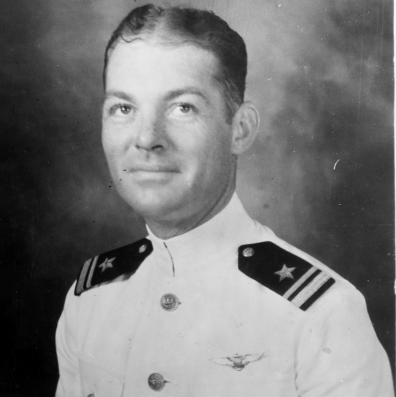A man wearing a white Navy uniform poses for a photo.