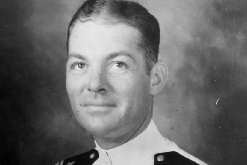 A man wearing a white Navy uniform poses for a photo.