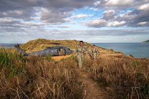 Two service members walk towards the camera, behind them is an HH-60W Jolly Green II helicopter.