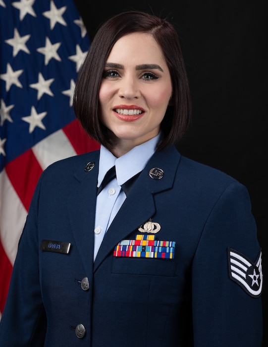 Official Photo of SSgt Ashley Huseby, Vocalist, United States Air Force Bands. SSgt Huseby is wearing navy blue service dress in front of an American flag.
