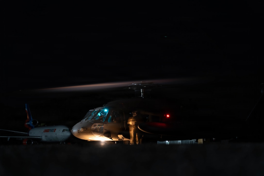 A soldier stands beside a military helicopter at night.