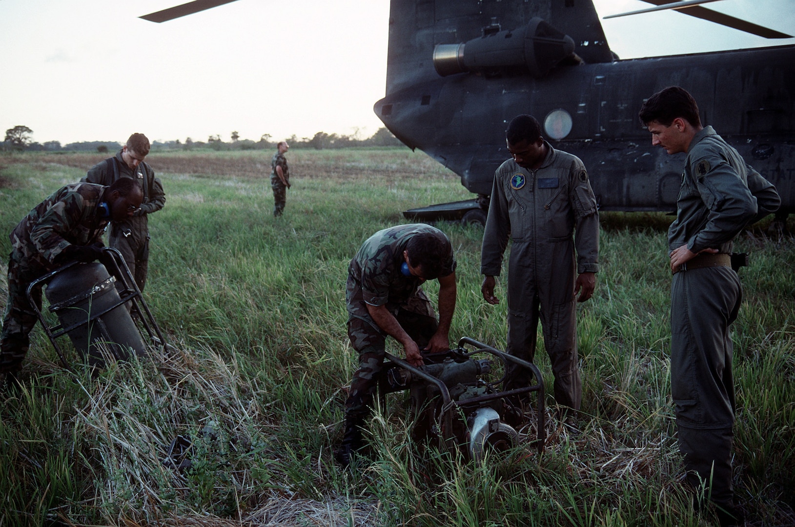 Soldiers stand in tall grass next to a Chinook helicopter