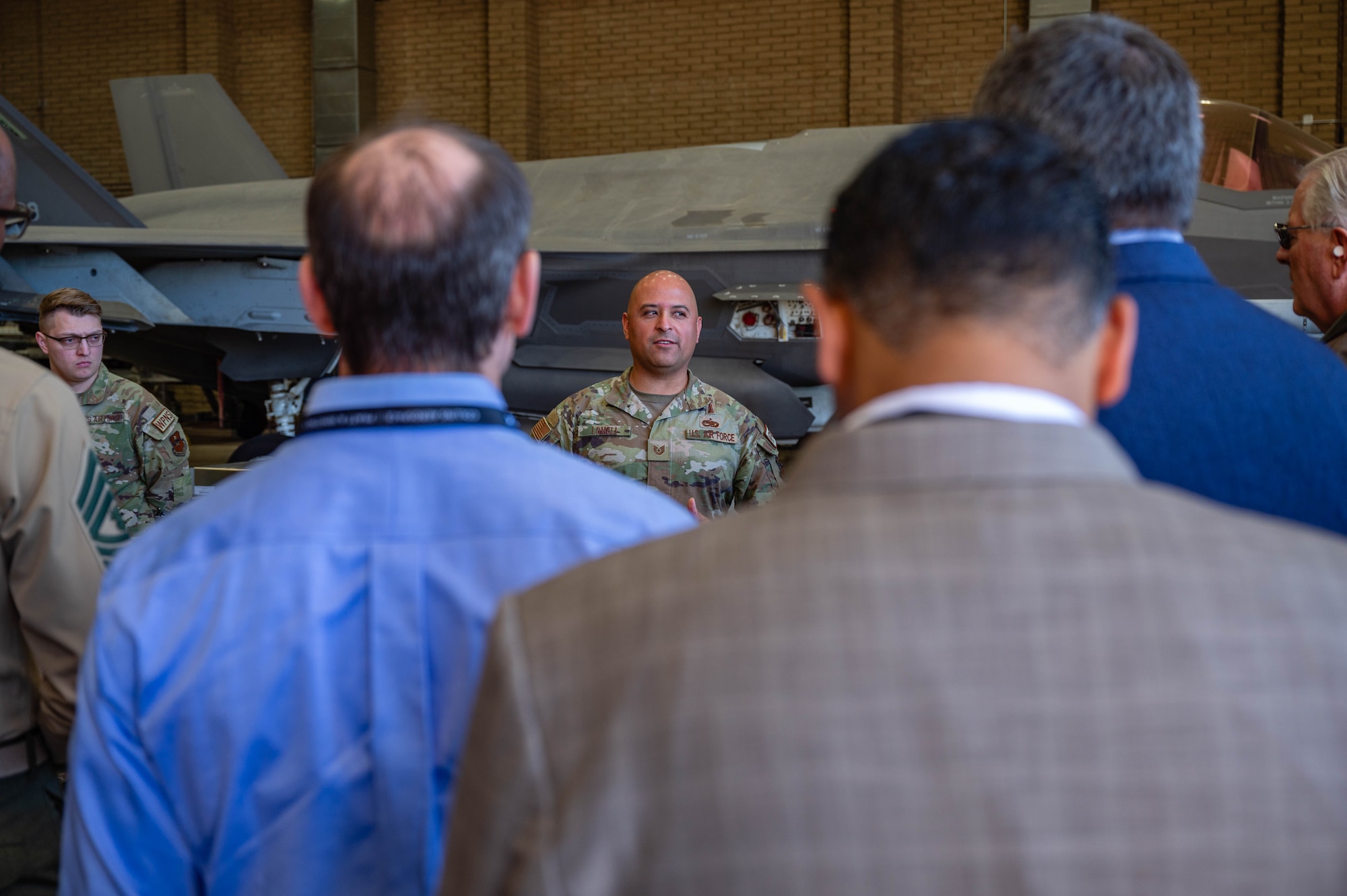 Members of the Department of War Maintenance Symposium, listen to U.S. Air Force Tech. Sgt. Diego Lomeli, 56th Component Maintenance Squadron loading standardization crew member, talk about the operations of the Aircraft Maintenance Units , Jan. 20, 2026, at Luke Air Force Base, Arizona.