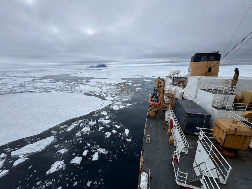 A large ship sails through icy water. There is a trail of broken ice behind the ship.
