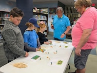 Mike Siekkinen (center), the Trident Refit Facility STEM Coordinator, and Jeff Chafin, a SWFLANT technical writer (right), guide students in assembling a rabbit-proof fence after a classroom reading of “The Tale of Peter Rabbit,” at the Camden County Public Library in Kingsland, Ga., on Jan. 21, 2026. The reading was part of SWFLANT’s Storybook STEM series, which offers K-12 students a unique opportunity to learn basic engineering principles from children’s books and understand how they apply to real-world Navy science and technology. (U.S. Navy photo provided)